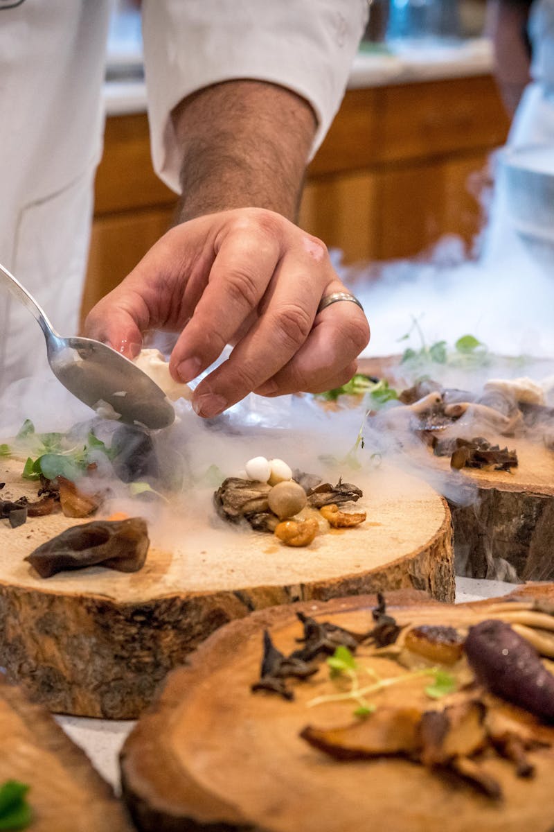 A chef artfully plating a gourmet dish with mushrooms and greens on wood slices.