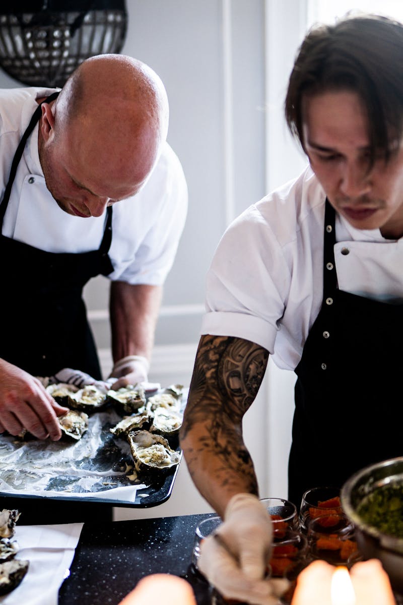 Two chefs in a restaurant kitchen preparing gourmet dishes with fresh ingredients and focused expressions.